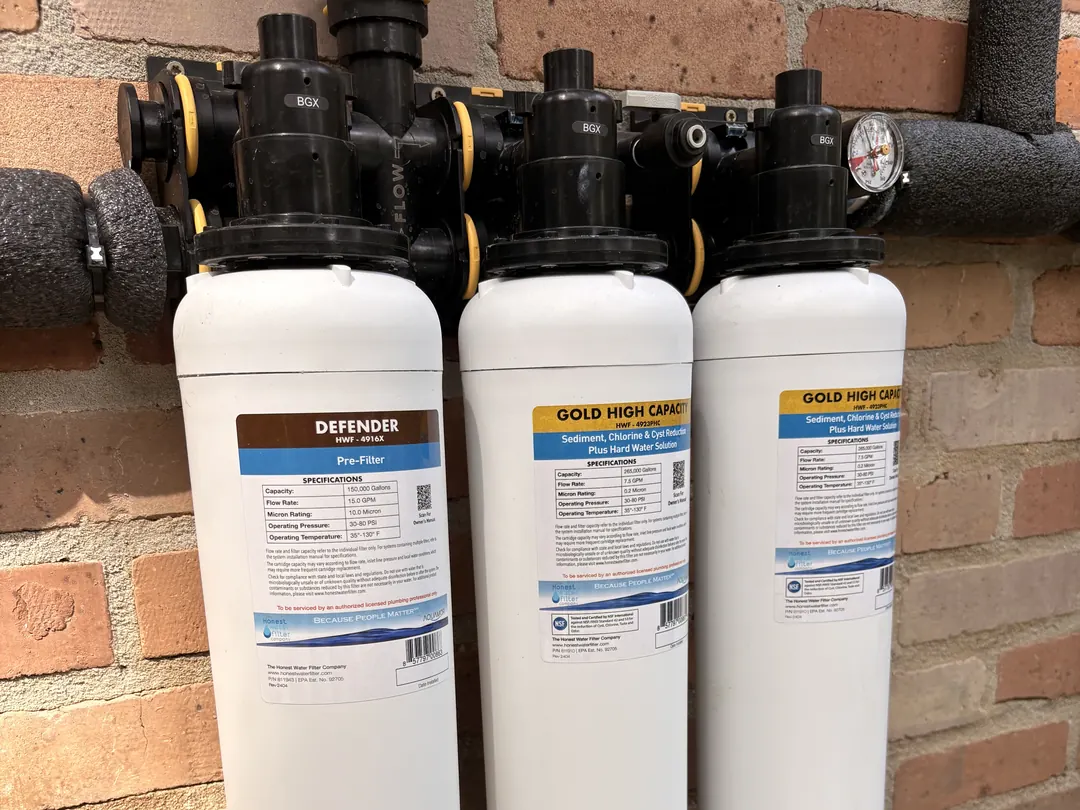 Apache Double Gold whole-home system in Baton Rouge: two banks of Defender pre-filter and Gold High Capacity cartridges on an exterior brick wall